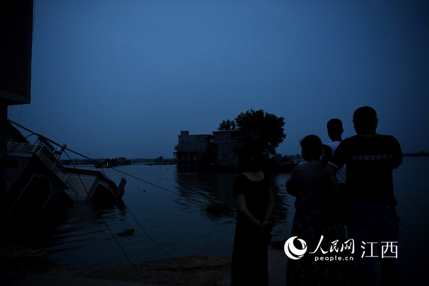在漫决处，几位村民站在岸边惋惜地看着倾倒在水中的房子。（人民网 时雨/摄）