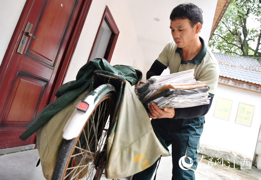 鄧六林將需要投遞的報紙、信件、包裹裝上自行車。（人民網 時雨攝）