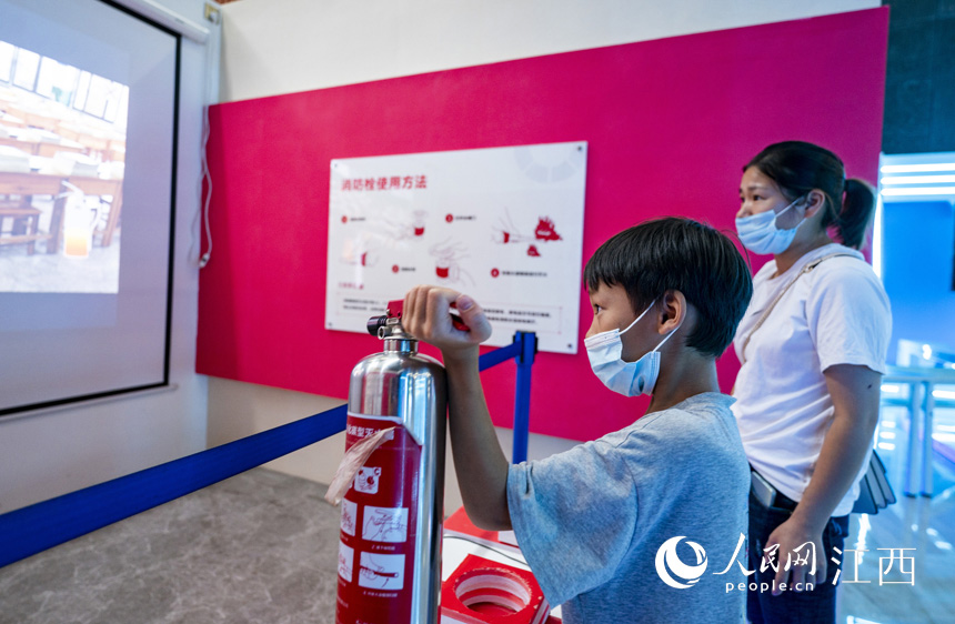 江西省新余市科技馆内，一名小朋友在家长陪同下体验虚拟灭火消防奇趣。赵春亮摄