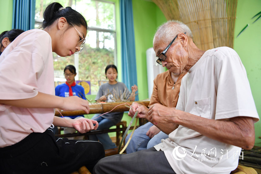 在蘆溪縣張佳坊學校，民間手藝人張友新正在教學生們竹篾編織。 人民網 時雨攝