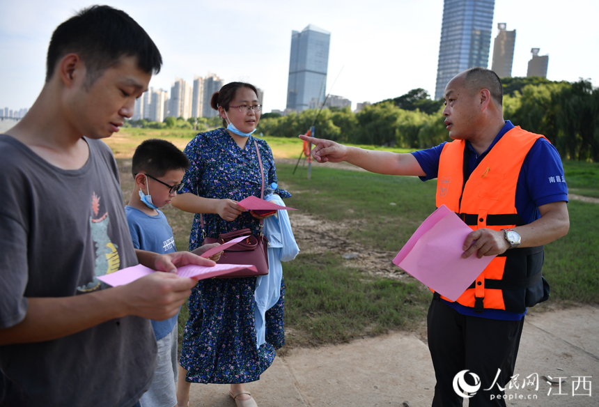 救援隊隊員正在贛江邊向市民發放防溺水宣傳資料。 人民網 時雨攝