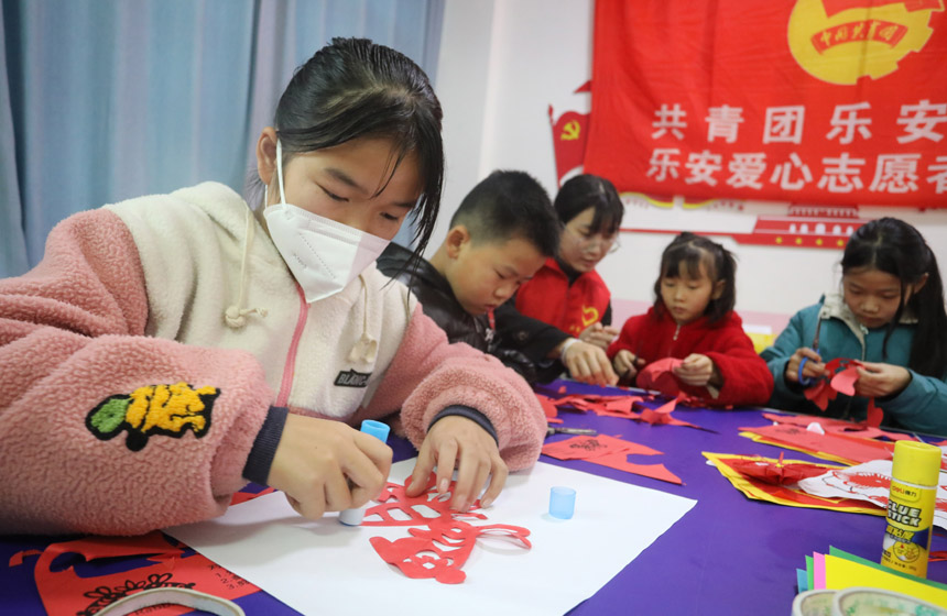 1月13日，在江西省抚州市乐安县惠民家园小区内，大学生自愿者正在和留守儿童们一起剪兔年手工窗花。邱志超摄
