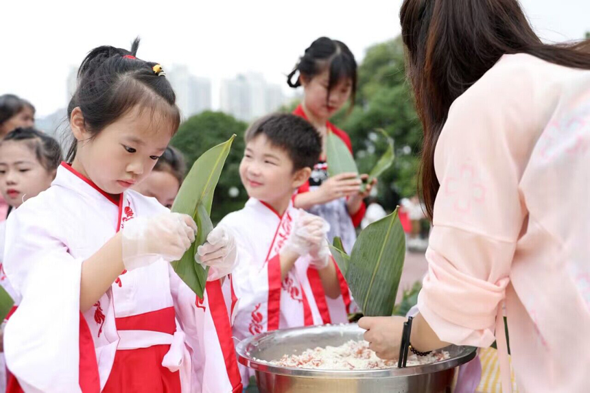 近日，江西省宜春市上高县镜山广场，县第二幼儿园的老师正在教孩子们包粽子。陈旗海摄