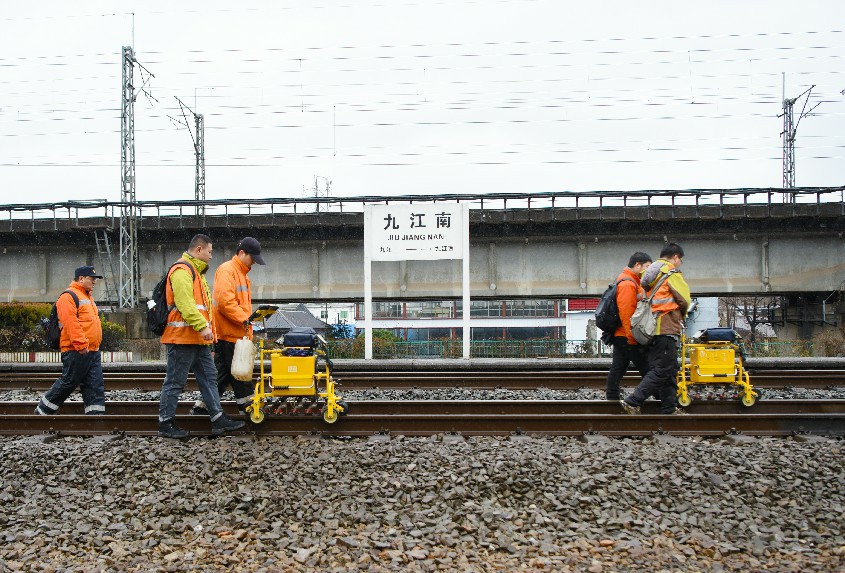 探伤人员推行钢轨探伤车行走在九江南站区铁路线路上。陈果摄