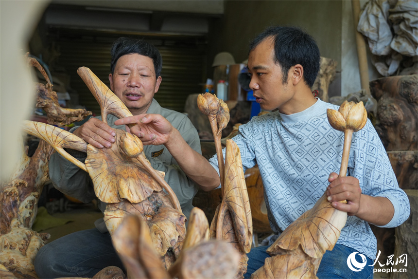 江西省级非遗项目根雕代表性传承人刘四喜在与徒弟交流雕刻技艺。人民网 孔文进摄