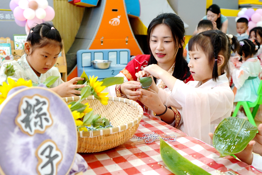 孩子们正在老师的指导下学包粽子。陈旗海摄