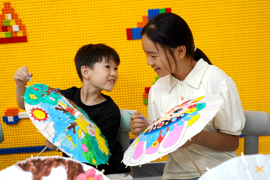 上高縣敖陽街道商城居委會轄區內的孩子們在志願者的指導下學習紙傘彩繪。陳旗海攝