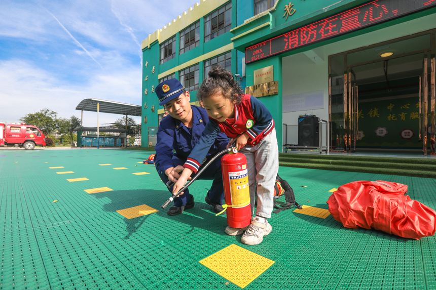 萍鄉市湘東區老關鎮中心幼兒園，消防員正指導小朋友們體驗消防器材使用方法。彭亮攝