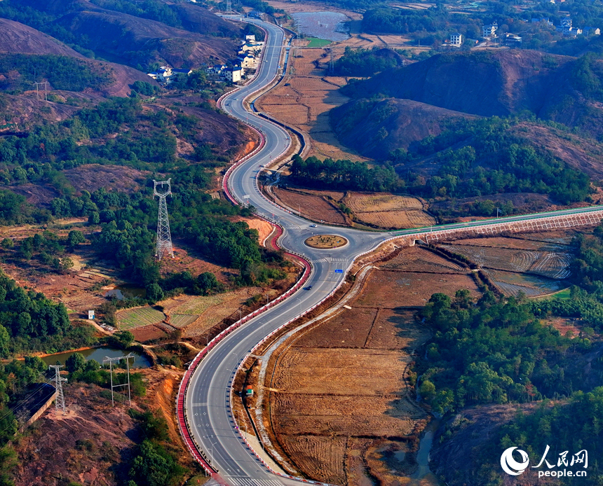 上饒市弋陽縣圭峰鎮，車輛在蜿蜒的公路上穿行，與沿線丹霞地貌山丘相映成景。人民網 朱海鵬攝