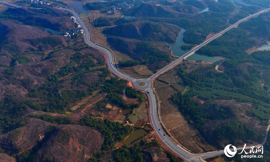 上饒市弋陽縣圭峰鎮，車輛在蜿蜒的公路上穿行，與沿線丹霞地貌山丘相映成景。人民網 朱海鵬攝