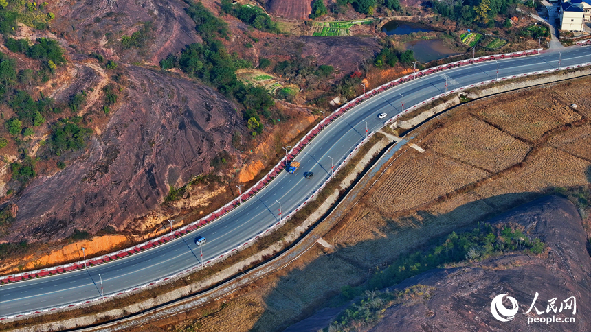 上饶市弋阳县圭峰镇，车辆在蜿蜒的公路上穿行，与沿线丹霞地貌山丘相映成景。人民网 朱海鹏摄