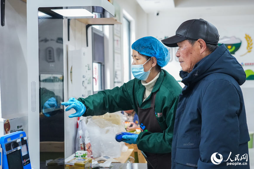 江西省南昌市東湖區光明社區幸福食堂，工作人員正在協助老人使用智能結算設備付款。人民網 孔文進攝