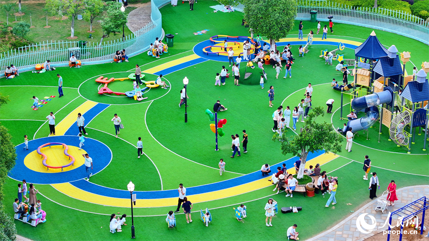 贛州市中心城區的一處公園裡，家長帶著孩子在兒童游樂園內游玩，樂享親子時光。人民網 朱海鵬攝