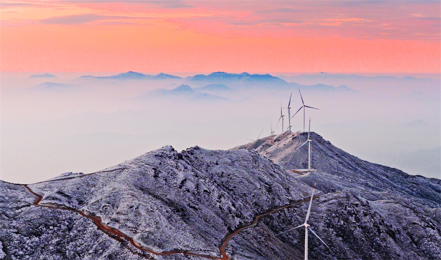 迎风旋转的风力发电机与多彩霞光、巍峨大山相映成景。康斌摄