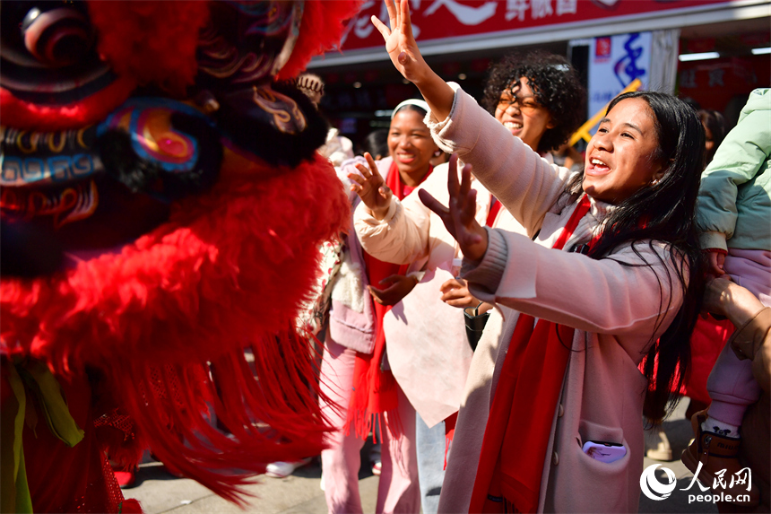 新洪城大市场内，留学生和舞狮表演者做互动游戏。人民网记者 时雨摄
