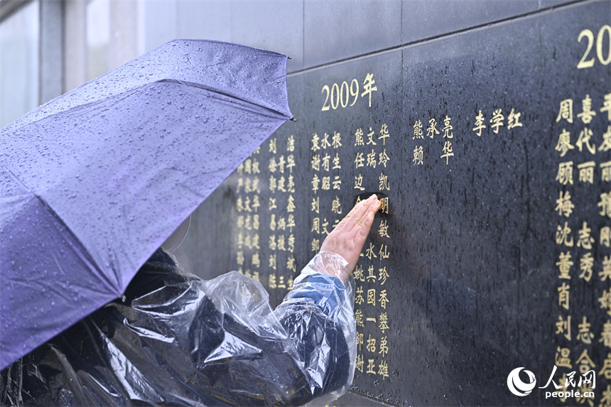 雨中，家属轻抚纪念墙上捐献者的姓名。人民网记者 时雨摄