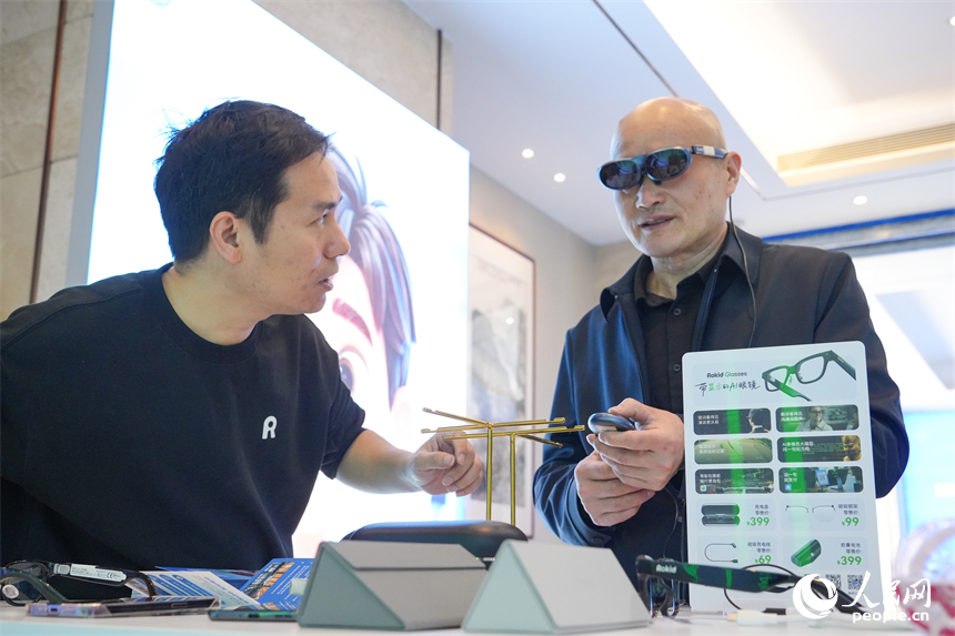 展台前，观众在工作人员指导下试戴智能眼镜。人民网 孔文进摄