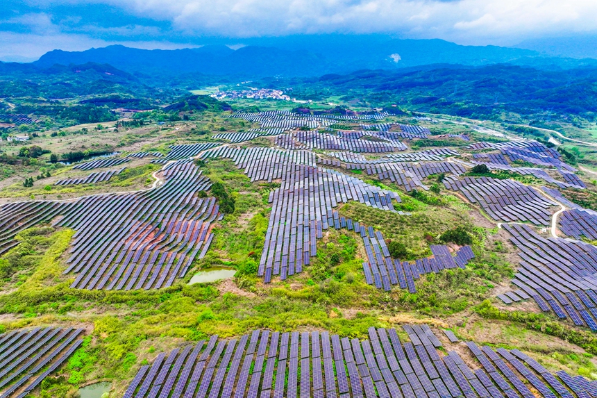 一塊塊光伏發電板整齊排列，與民居、山巒交相輝映。