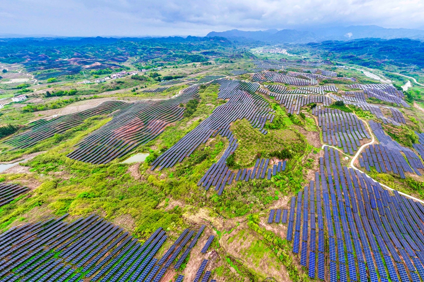 一块块光伏发电板整齐排列，与民居、山峦交相辉映。